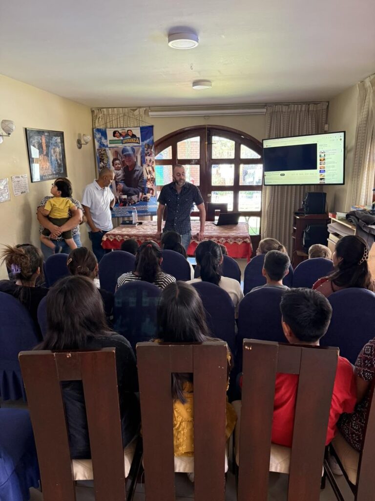 Tim Daviscourt teaching the girls in the living room of the RCI home, with Tony Velez listening at the side