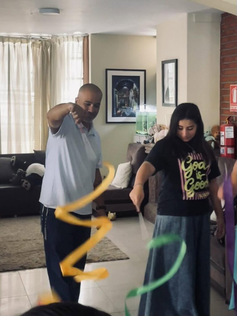 Tony Velez twirling a yellow ribbon beside one of the girls in the living room