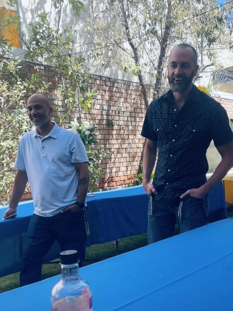 Tony Velez and Tim Daviscourt laughing beside the blue tables in the garden before the feast