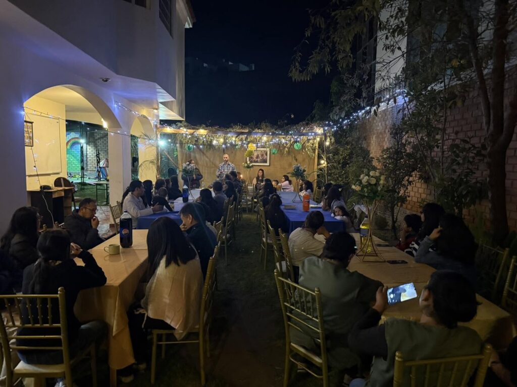 The garden full of guests seated at the tables under the lights for the final night of Sukkot