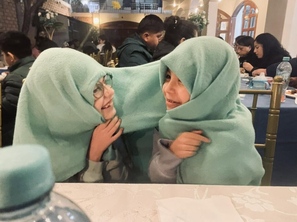 Two girls wrapped in a green blanket laughing together at the table
